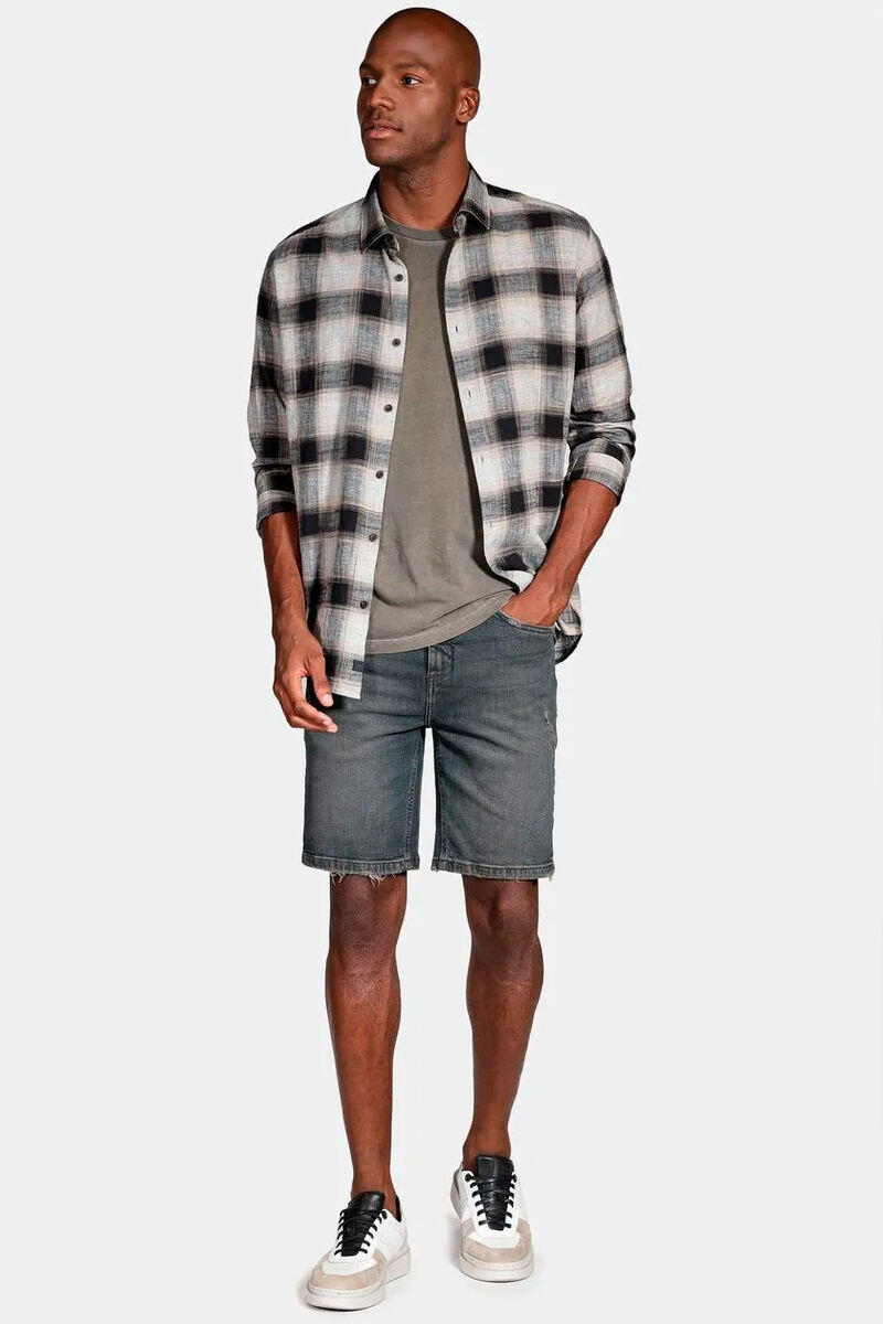 modelo usando uma camiseta básica bege uma camisa xadrez sobreposta e uma bermmuda jeans em um funod branco 