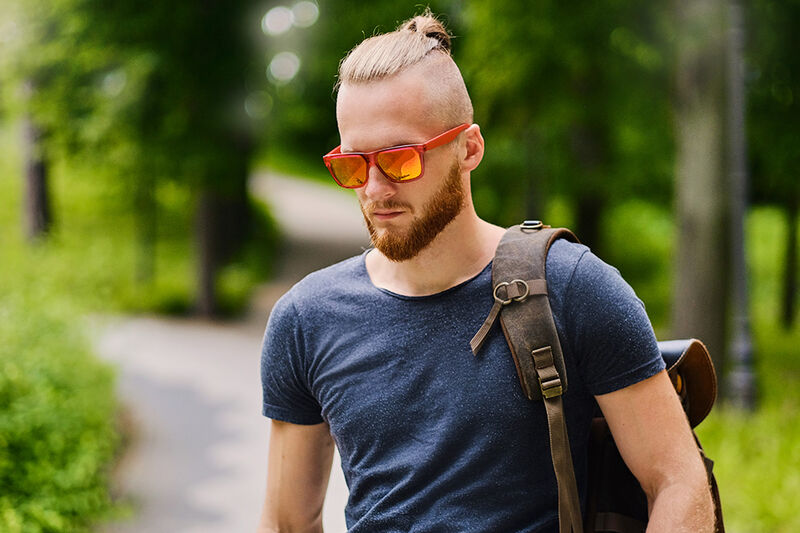 homem ruivo em um parque usando óculos escuros com o corte undercut com coque
