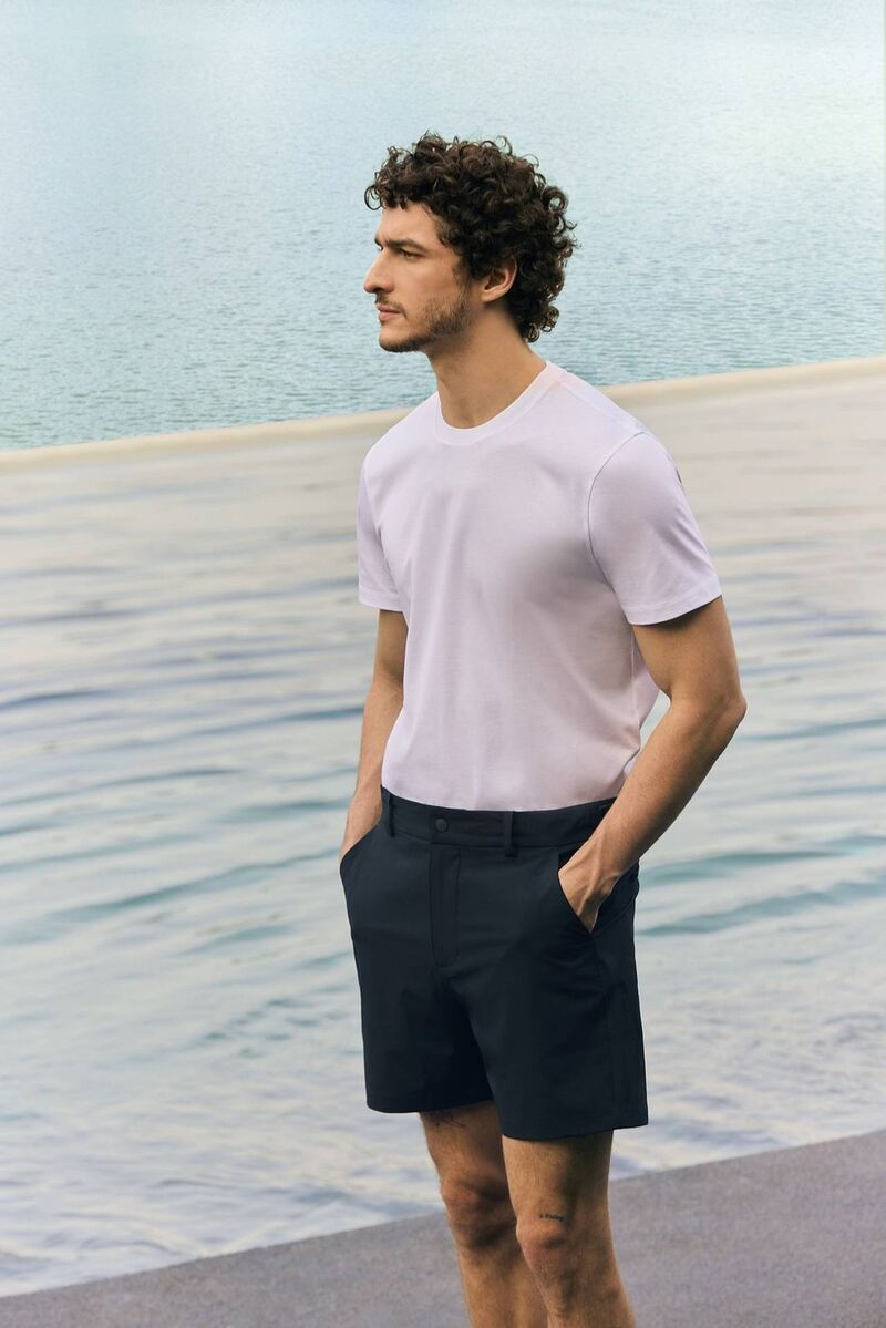 modelo na praia usando camisa e bermuda em um por do sol