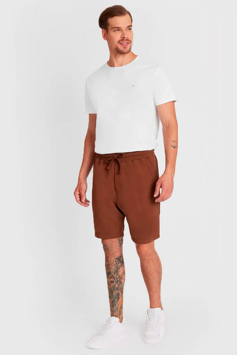 modelo usando uma bermuda de moletom na cor ferrugem e uma camiseta branca em um fundo branco