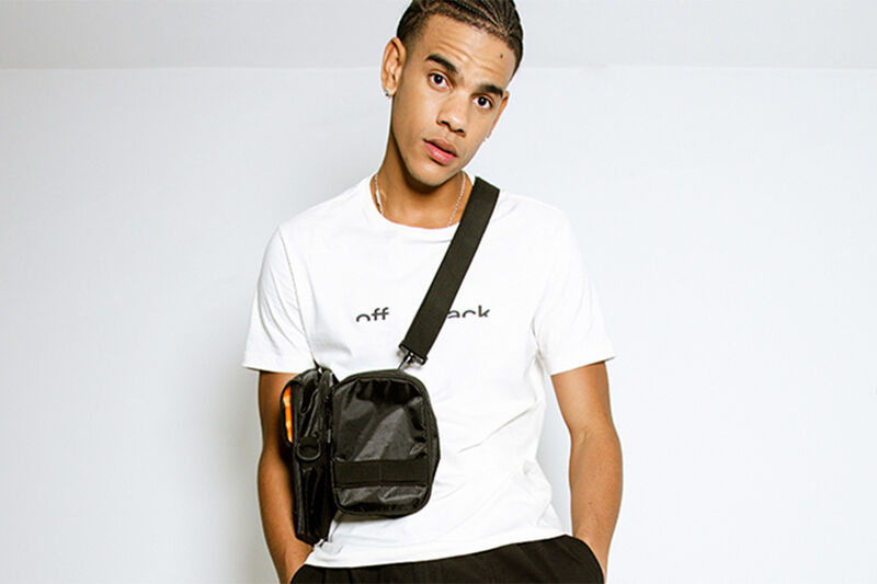 modelo usando uma camiseta branca com estampa na frente e uma bolsa transversal em um fundo claro