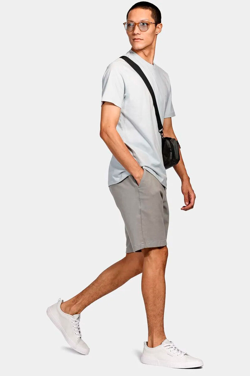 modelo usando uma camiseta branca, uma bermuda bege e bolsa transversal em um fundo branco 