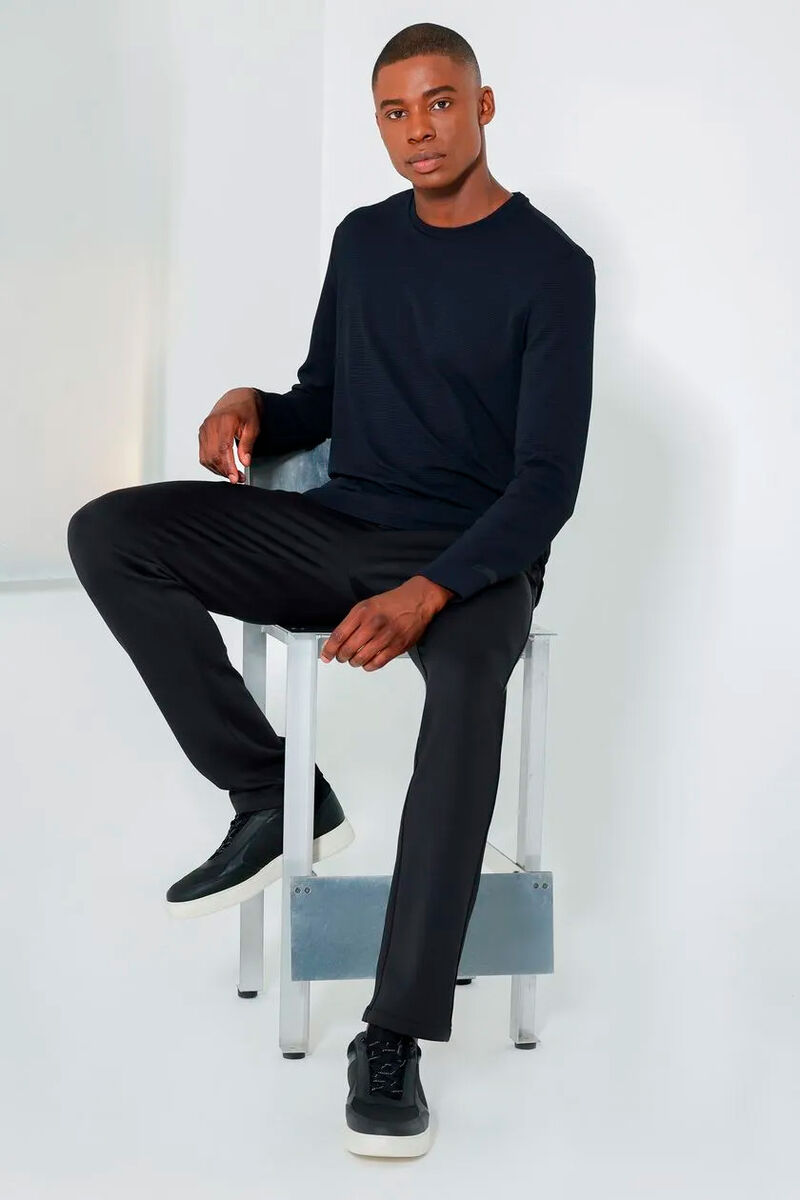 modelo usando uma camiseta de manga longa e calça chino sentado em uma cadeira em um fundo branco