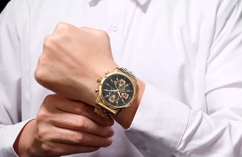 Relógio de pulso dourado em braço masculino.