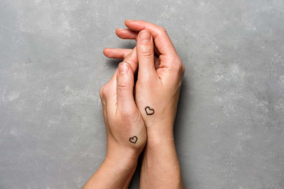 Duas mãos unidas com tatuagens de corações