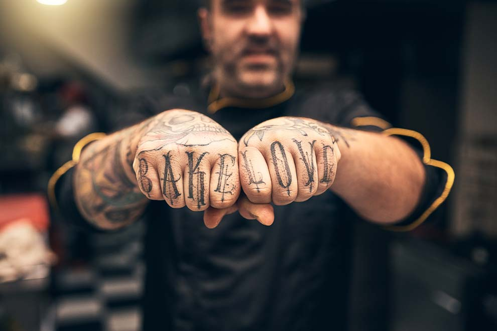Chef com tatuagens nas mãos exibindo 'Bake Love'