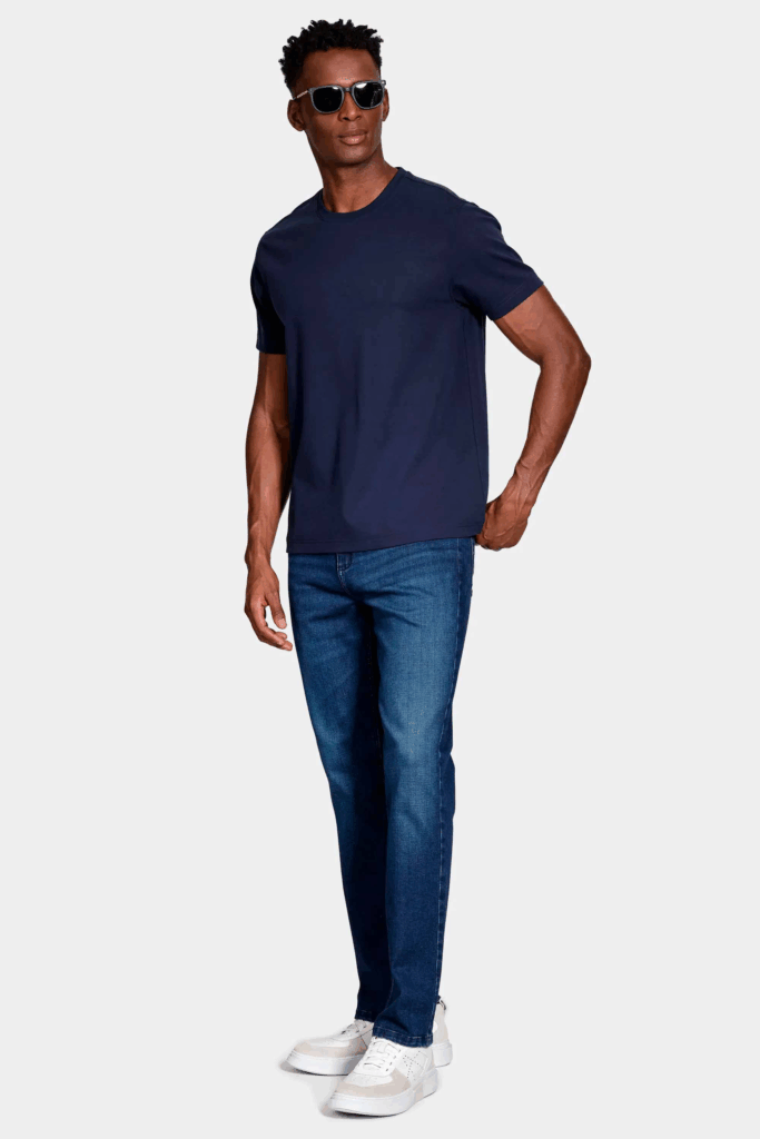 Homem com camiseta azul e jeans em pé, usando óculos de sol