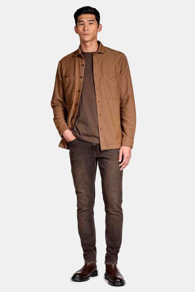 modelo masculino usando uma camisa preta, jaqueta bege e calça jeans em um fundo branco 