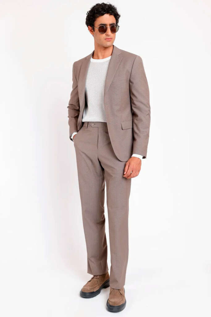 modelo masculino usando um sueter branco, blazer e calça de alfaiataria cinza em um fundo branco 