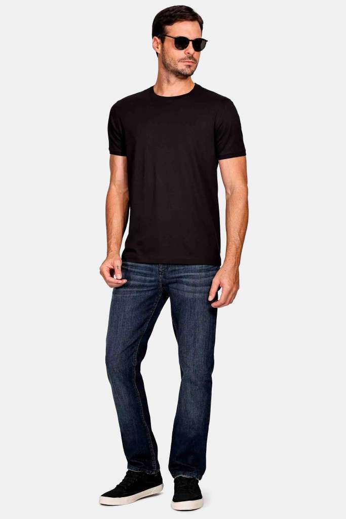modelo masculino usando uma camiseta preta de algodão pima e uma calça jeans junto de um tenis simples em um fundo branco 