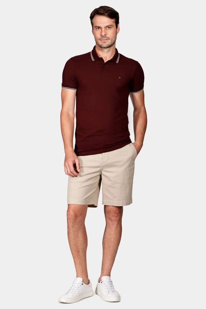 bermuda e polo modelo masculino usando uma camisa polo vermelha e uma bermuda junto de um tenis branco casual em um fundo branco