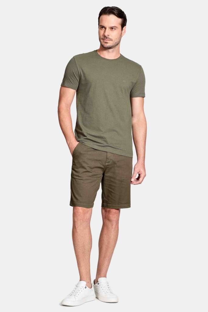 camisa dry fit e bermuda modelo masculino usando uma camisa dry fit verde militar e uma bermuda verde com um tenis casual em um fundo branco