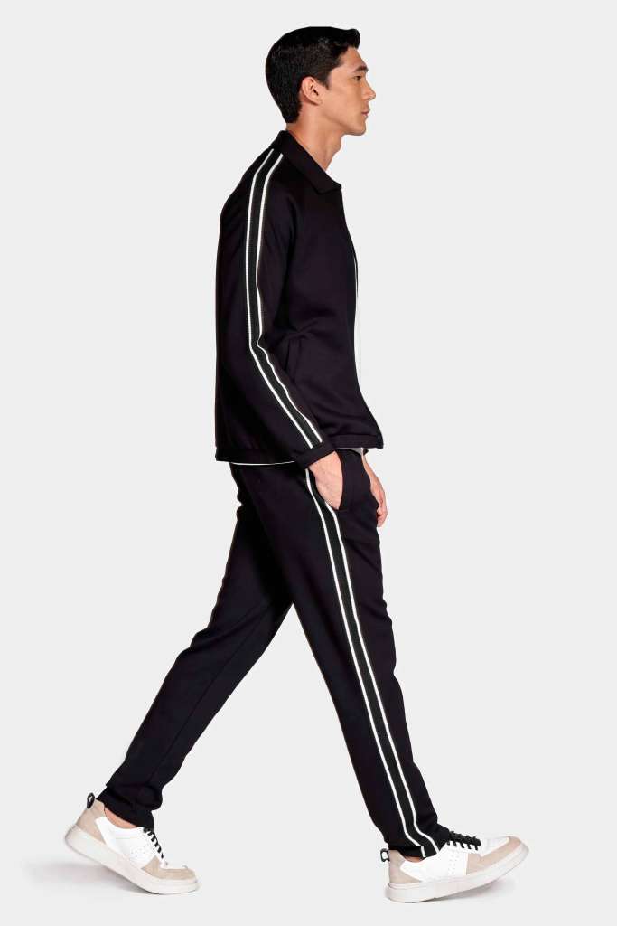 moletom e camisa over modelo masculino usando usando uma camisa branca e um conjunto de moletom preto e tenis em um fundo branco