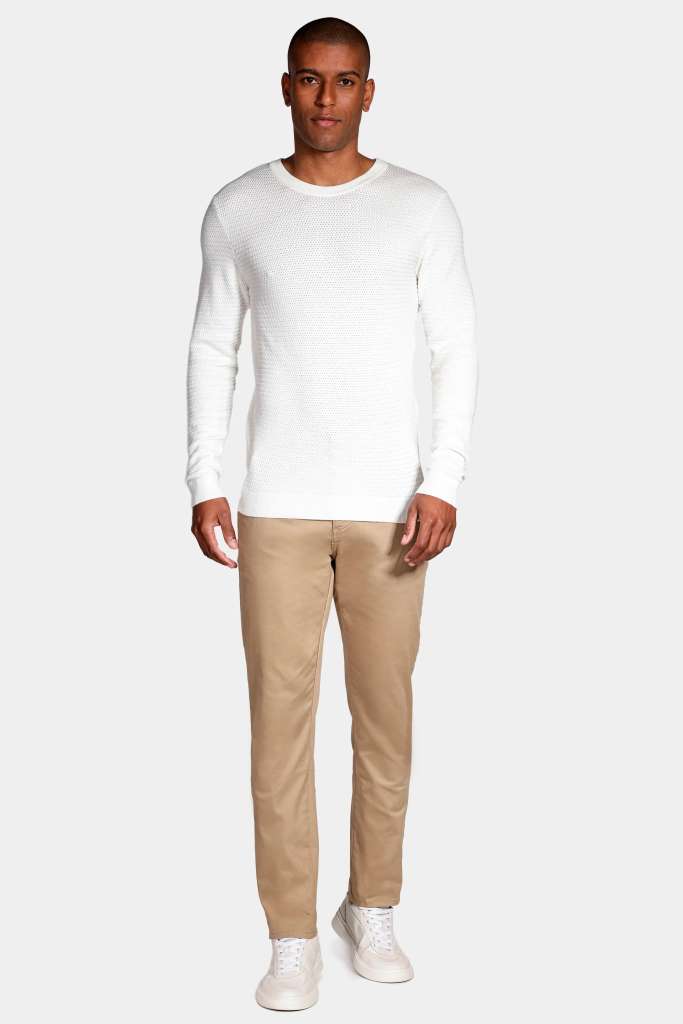 modelo masculino usando uma camisa de manga longa em tricot leve e uma calça alfaiataria bege em um fundo branco 