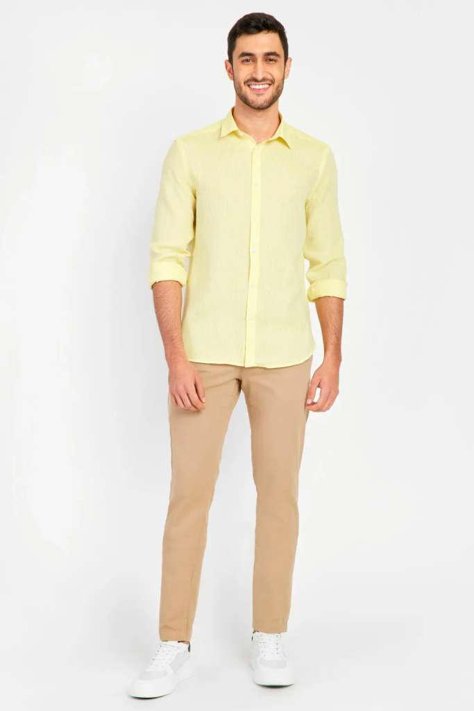 modelo masculino usando uma camisa de linho amarela e uma calça marrom em um fundo branco 