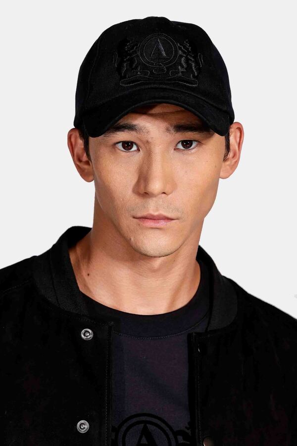 um modelo masculino usando um bone preto, uma camiseta preta e com uma  camisa de sobreposição em um fundo branco 