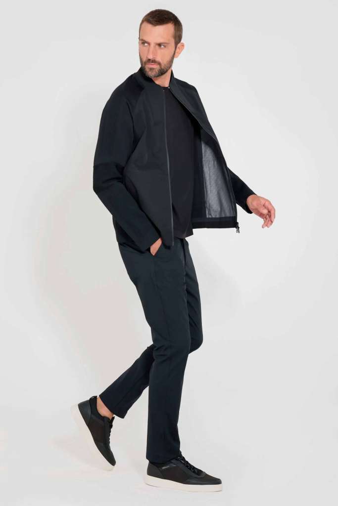 modelo masculino usando uma camisa preta junto de uma jauqeta preta e calça jeans escura em um fundo branco 