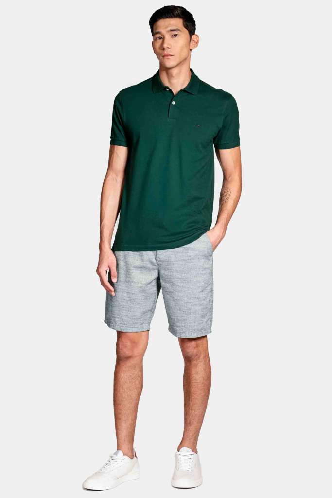 modelo masculino usando uma camisa polo verde e uma bermuda clara em um fundo branco 