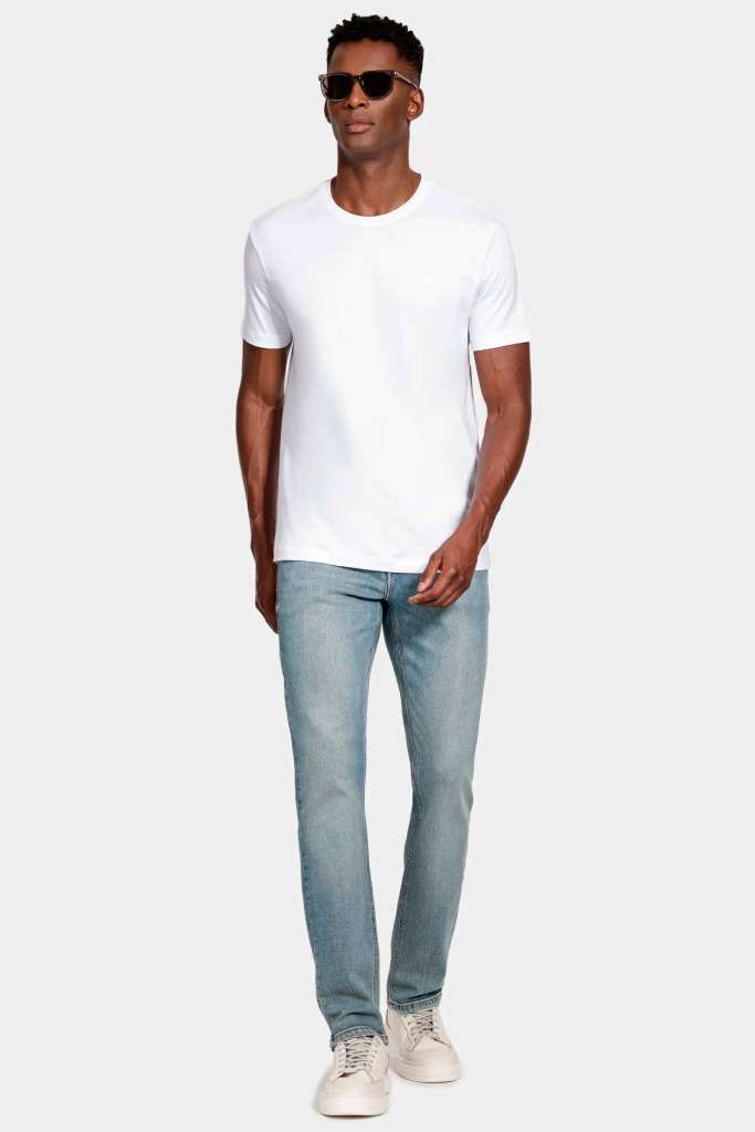 modelo masculino usando uma camiseta branca básica e calça jeans, junto de tenis claro e um fundo branco 